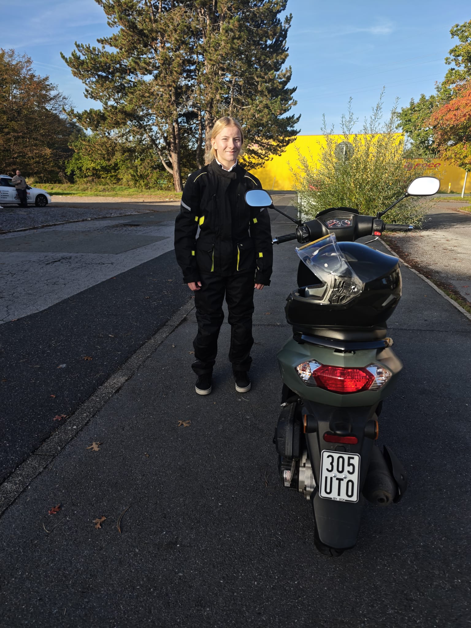 Maike in Schutzkleidung neben dem Motorroller der Fahrschule nach bestandener Prüfung