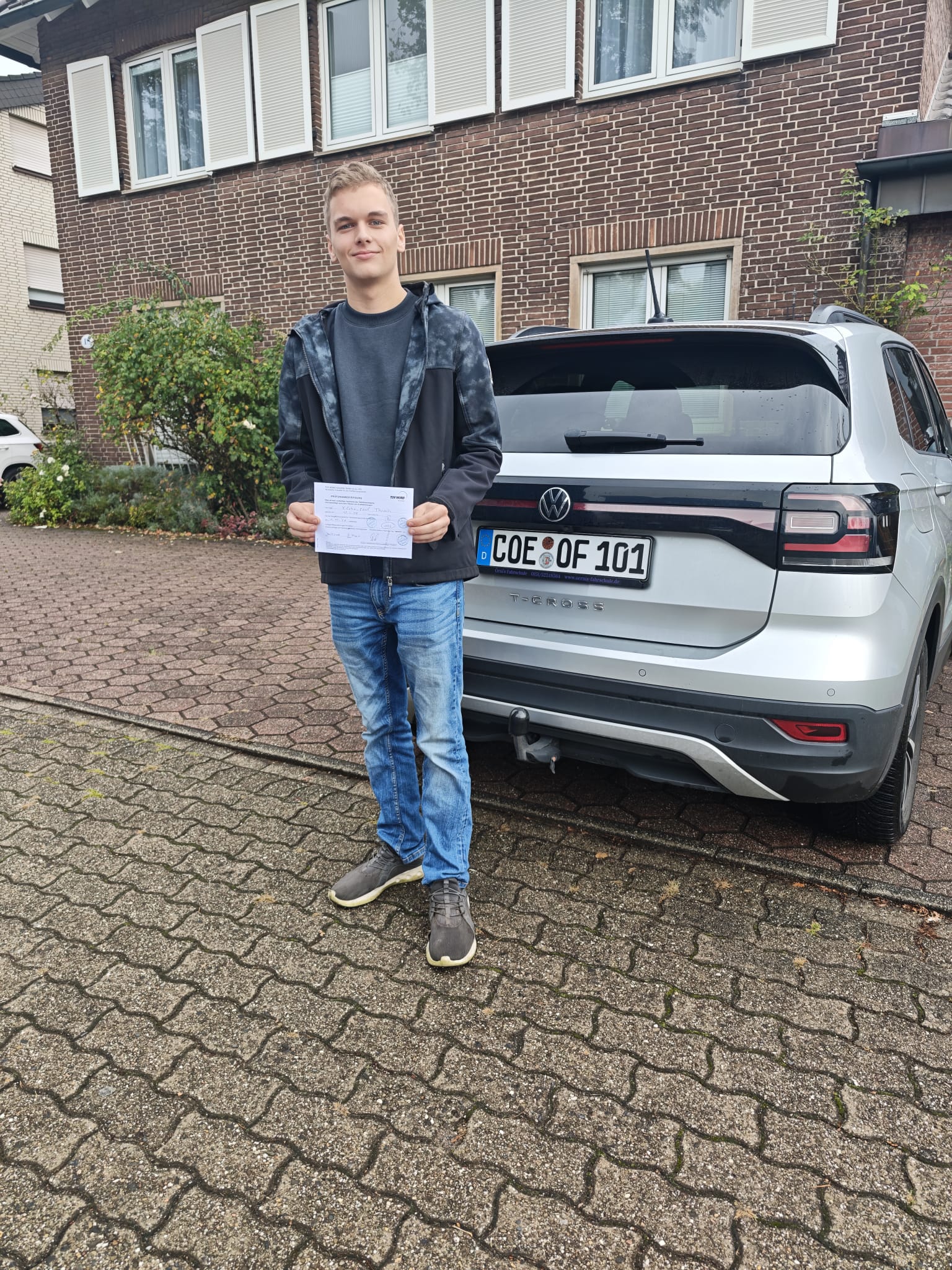 Paul mit seiner bestandenen Prüfung vor dem VW T-Cross der Fahrschule